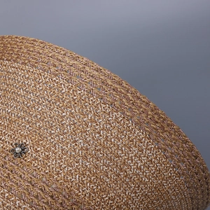 Detail of woven straw sun hat featuring a silver flower ornament and pearly bead accent