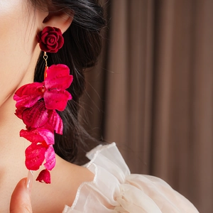 Détail de boucles d'oreilles fleurs en velours rouge avec franges en tissu sur modèle