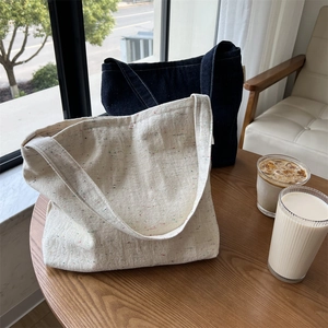 Dettaglio di borse tote minimaliste in denim e tela su un tavolo di legno in un caffè