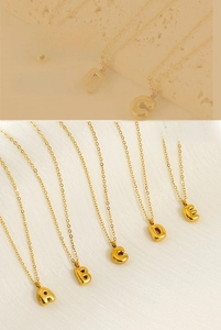 Macro detail of golden bubble letter necklaces on stone and satin background textures