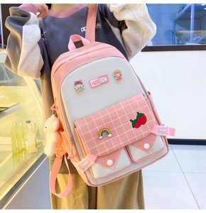 Detail of pink and beige student backpack with cute badges and a plush bear pendant