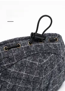 Detail of adjustable drawstring buckle and metal eyelet on grey plaid winter beret