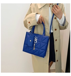 Sac à main bleu matelassé avec mini pochette et pampille porté sur un trench-coat