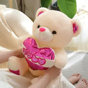 Cream teddy bear plush holding a pink metallic LOVE heart, soft long-hair texture toy