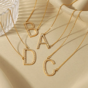Gold-plated 18K stainless steel initial necklaces with diamonds on beige silk backdrop