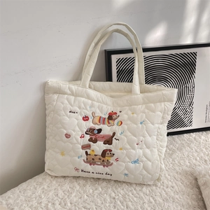 Detail of cream quilted tote bag featuring colorful cute dog embroidery and heart patterns