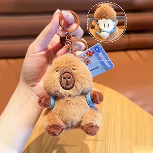 Detail of plush capybara keychain with blue backpack and metal ring on wooden table