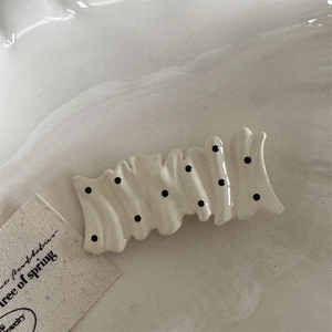 Close-up of a wavy cream hair clip with black polka dots on a textured background