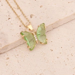 Detail of a gold butterfly necklace with green crystal and zircon stones on a beige stone