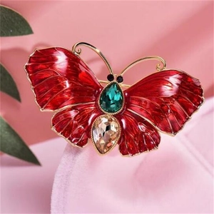 Détail d'une broche papillon en émail rouge avec cristal émeraude et dorure élégante