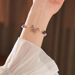 Detail of butterfly bracelet with purple zircon and white pearls on female wrist