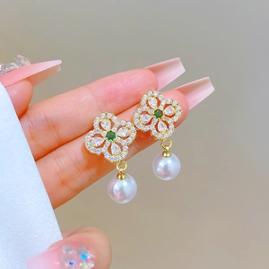 Detail of gold clover earrings with green center stones and hanging white pearls