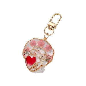 Handmade resin keychain with pink dried flowers and gold metal face outline on white background