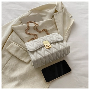 Macro detail of white quilted crossbody bag with golden clasp and chain on a blazer