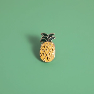 Macro detail of a pineapple enamel brooch with yellow body and green metal leaves