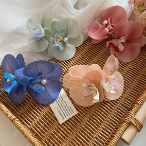 Detail of fabric orchid hair clips with pearls on a woven tray with white gauze background