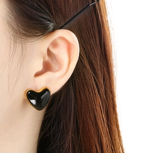 Close-up of heart-shaped black enamel stud earring with gold border worn by a model