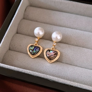Détail de boucles d'oreilles cœur en perle avec nacre bordée d'or et accents de zircon