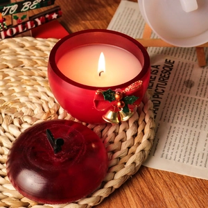 Gros plan sur un pot de bougie en forme de pomme rouge avec cloche de Noël et fini mat
