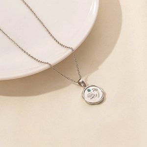 Macro shot of a silver necklace with wave-edge round pendant showing baby footprints and blue stone