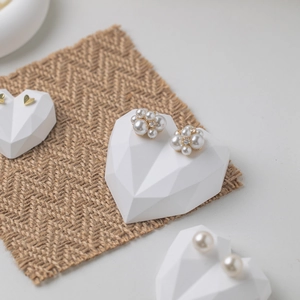 Elegant pearl flower and heart earrings displayed on a textured linen jewelry prop stand