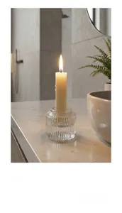Portacandele in vetro scanalato con candela a stelo accesa su piano di marmo bianco