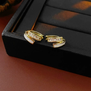 Vue macro de boucles d'oreilles dorées avec zircons et finition en émail blanc