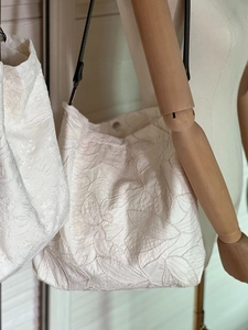 Detail of embroidered tote bag featuring white floral patterns and slim black shoulder straps