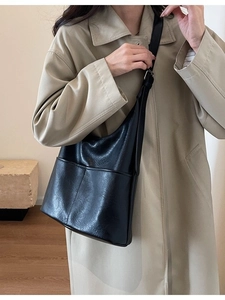 Minimalist black leather tote bag shown on model with classic trench coat