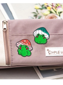 Macro view of cute cartoon enamel frog pins with mushroom hats on a purple bag pocket