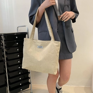 Detail view of large corduroy tote bag in beige with fashion label for daily use