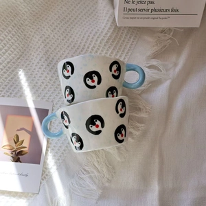 Close-up of stacked ceramic mugs with penguin patterns on a soft white blanket