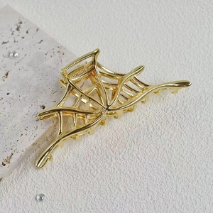 Close-up of golden metal spider web hair claw clip with polished finish on white stone
