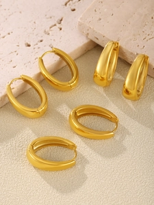 Macro view of several chunky oval gold plated stainless steel hoop earrings on stone