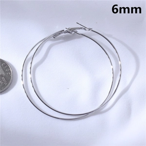 Detailed view of silver hoop earrings next to a coin showing the 6mm thickness scale