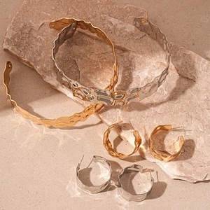 Modern wavy metal jewelry set including gold and silver textured cuff bracelets and earrings