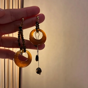 Detail of amber resin tiger eye earrings featuring asymmetric round bead drop design