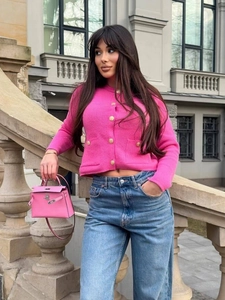 Chic pink knit cardigan with gold buttons paired with jeans in a stylish outdoor setting