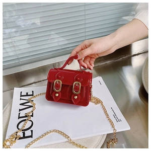 Close-up of a red glossy mini jelly handbag with dual buckles and a fine gold chain strap