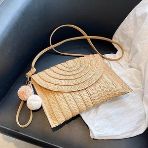 Borsa a tracolla in paglia intrecciata beige con pompon decorativi su sedia in pelle