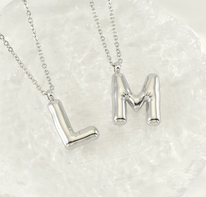 Macro detail of glossy stainless steel puffy bubble letter L and M pendants on fine chains