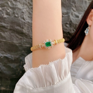 Macro shot of luxury gold mesh bracelet with emerald green stone and pavé diamonds