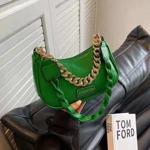 Green crescent hobo bag with chunky gold chain and braided handle on black sofa