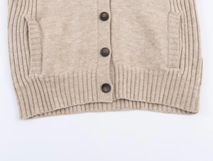 Detail view of beige knit cardigan with dark resin buttons and ribbed hem texture