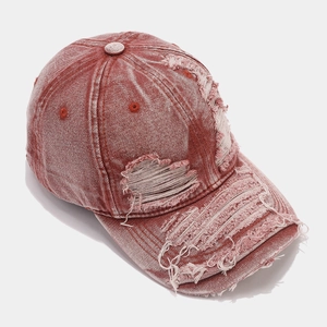 Close-up of vintage distressed burgundy denim baseball cap with frayed edges and torn details