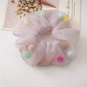 Close-up of a light purple mesh scrunchie filled with colorful soft pom-poms on a white surface