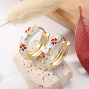 Macro detail of sky blue enamel hoop earrings with red floral patterns and gold accents