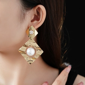 Macro detail of geometric gold earrings featuring a white pearl and sparkling zircon stone