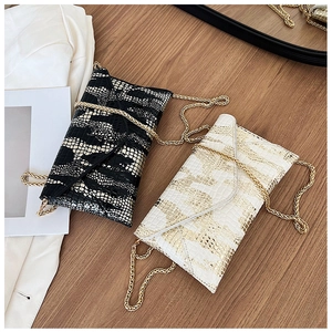 Detail of black and beige crocodile pattern envelope chain bags on a wooden table