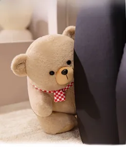 Close-up of milk tea colored teddy bear with red plaid scarf peeking from behind a sofa